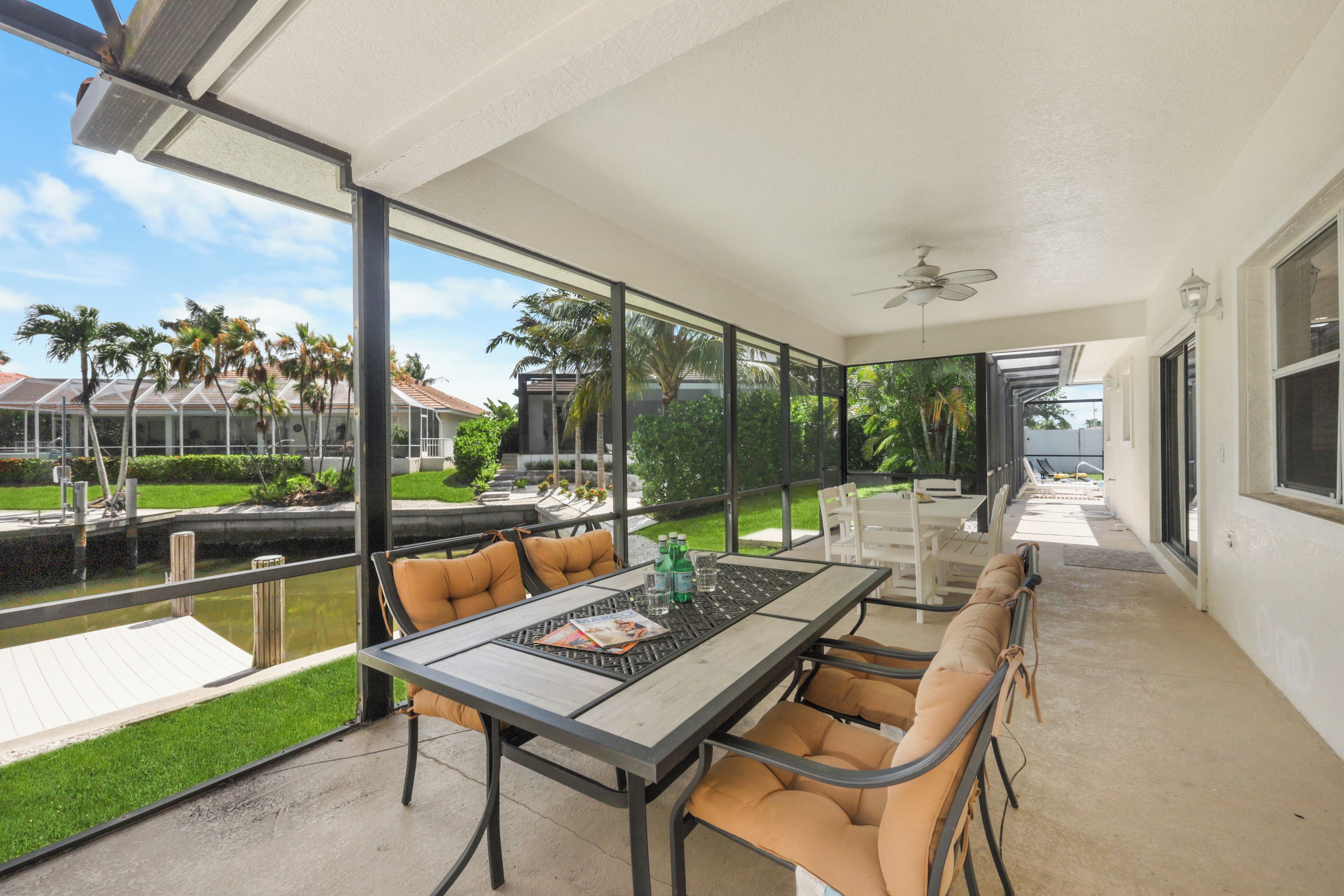 A covered patio area with a table and chairs, a view of the water, and a building in the background.