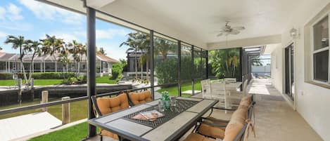 A covered patio area with a table and chairs, a view of the water, and a building in the background.