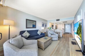 A modern living room with a sofa, armchairs, a coffee table, and a TV. - Charming Beachfront Condo | Pool, Spa & Views (Marco Island)