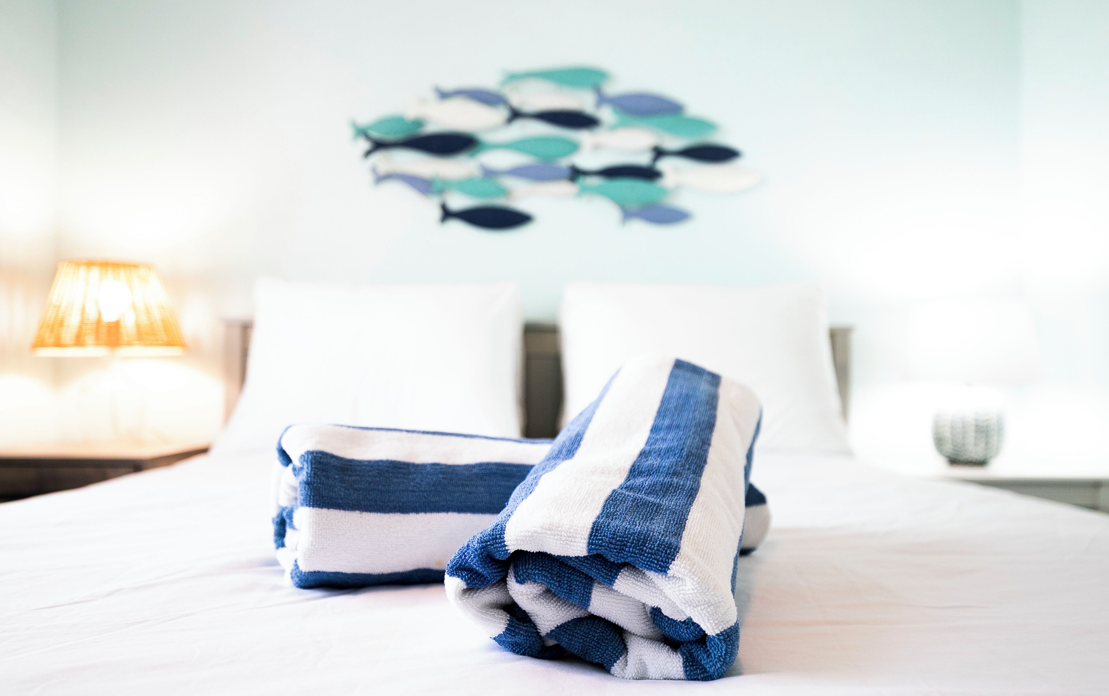 Cama bem arrumada com toalhas dobradas e uma arte na parede de peixes.