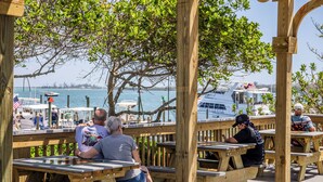 Un muelle de madera con mesas de picnic y vistas a un puerto deportivo con barcos.