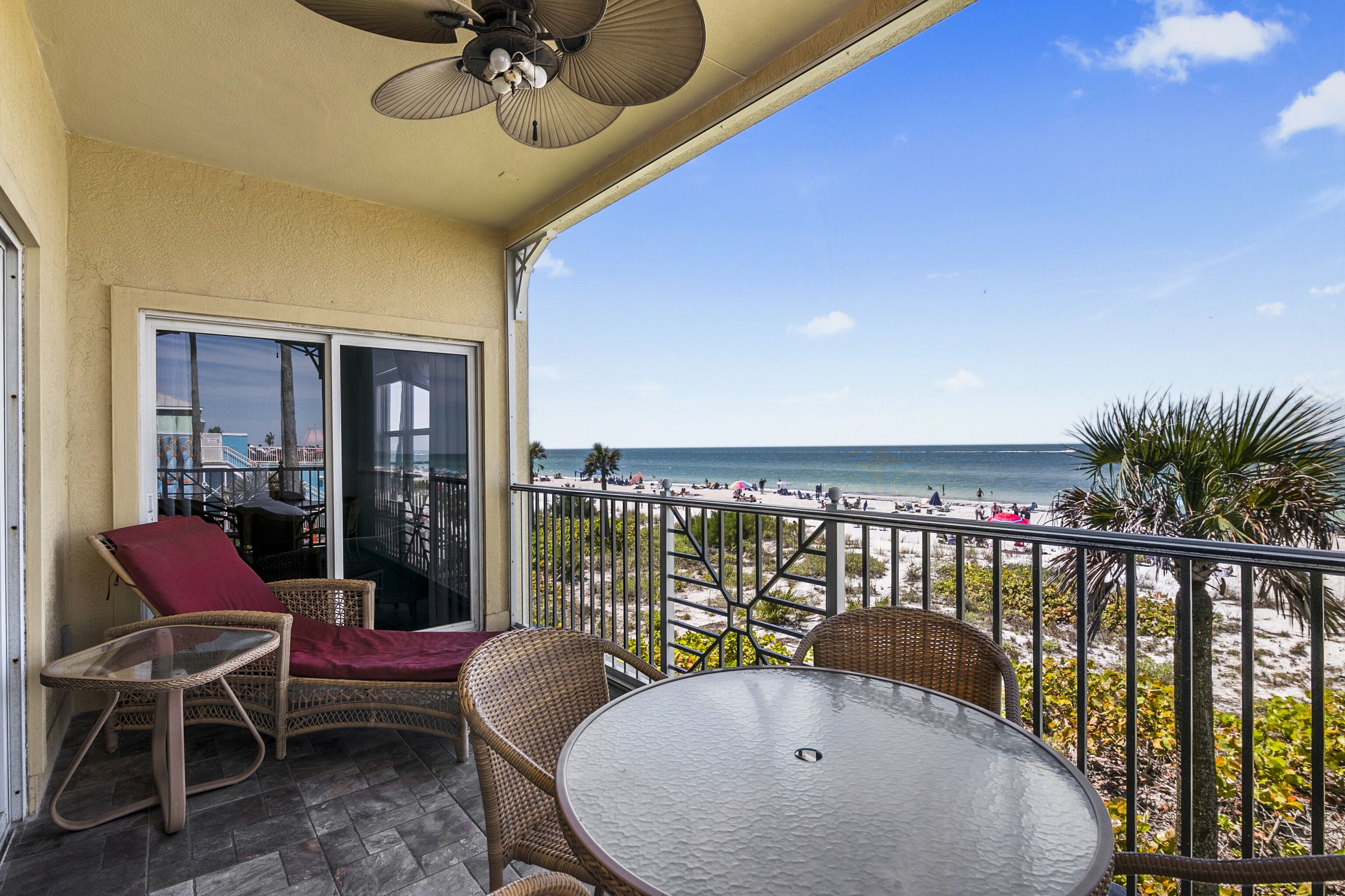 A balcony with wicker furniture, a glass table, and a view of the beach.