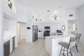 A modern kitchen with white cabinetry, stainless steel appliances, and a central island with bar stools.