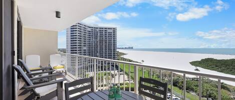 A balcony with a table, two chairs, and a view of a body of water and buildings.