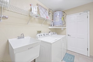 A laundry area with two front-loading washing machines, a white sink, and a water heater on a shelf. - Pet-friendly Waterfront | Pool & Steps to Beach (Marco Island)