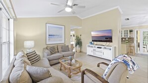 A spacious living room with a large sofa, a coffee table, and a television. There is a ceiling fan, a window, and a view of the outside. - Pet-friendly Waterfront | Pool & Steps to Beach (Marco Island)