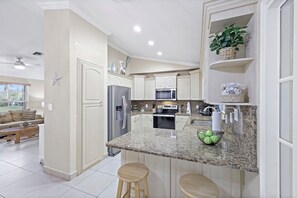 A modern kitchen with granite countertops, stainless steel appliances, and a central island with stools. - Pet-friendly Waterfront | Pool & Steps to Beach (Marco Island)