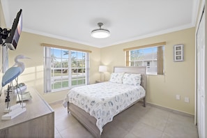 A bedroom with a bed, a desk with a computer, a lamp, and a window with a view of palm trees. - Pet-friendly Waterfront | Pool & Steps to Beach (Marco Island)