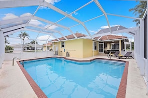 A swimming pool with a covered area, a yellow building, and a patio with chairs. - Pet-friendly Waterfront | Pool & Steps to Beach (Marco Island)