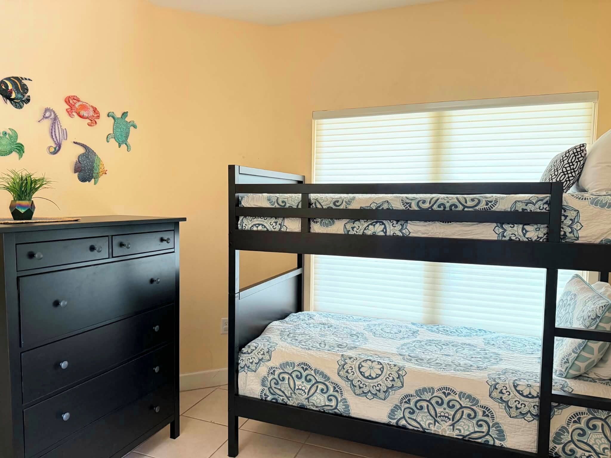 A bunk bed with patterned bedding, a dresser with multiple drawers, and a wall with colorful fish decals.