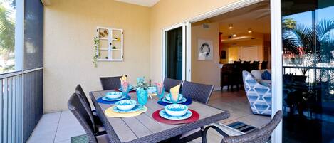 A dining area with a table set for four, surrounded by wicker chairs, and a sliding glass door leading to a dining room.