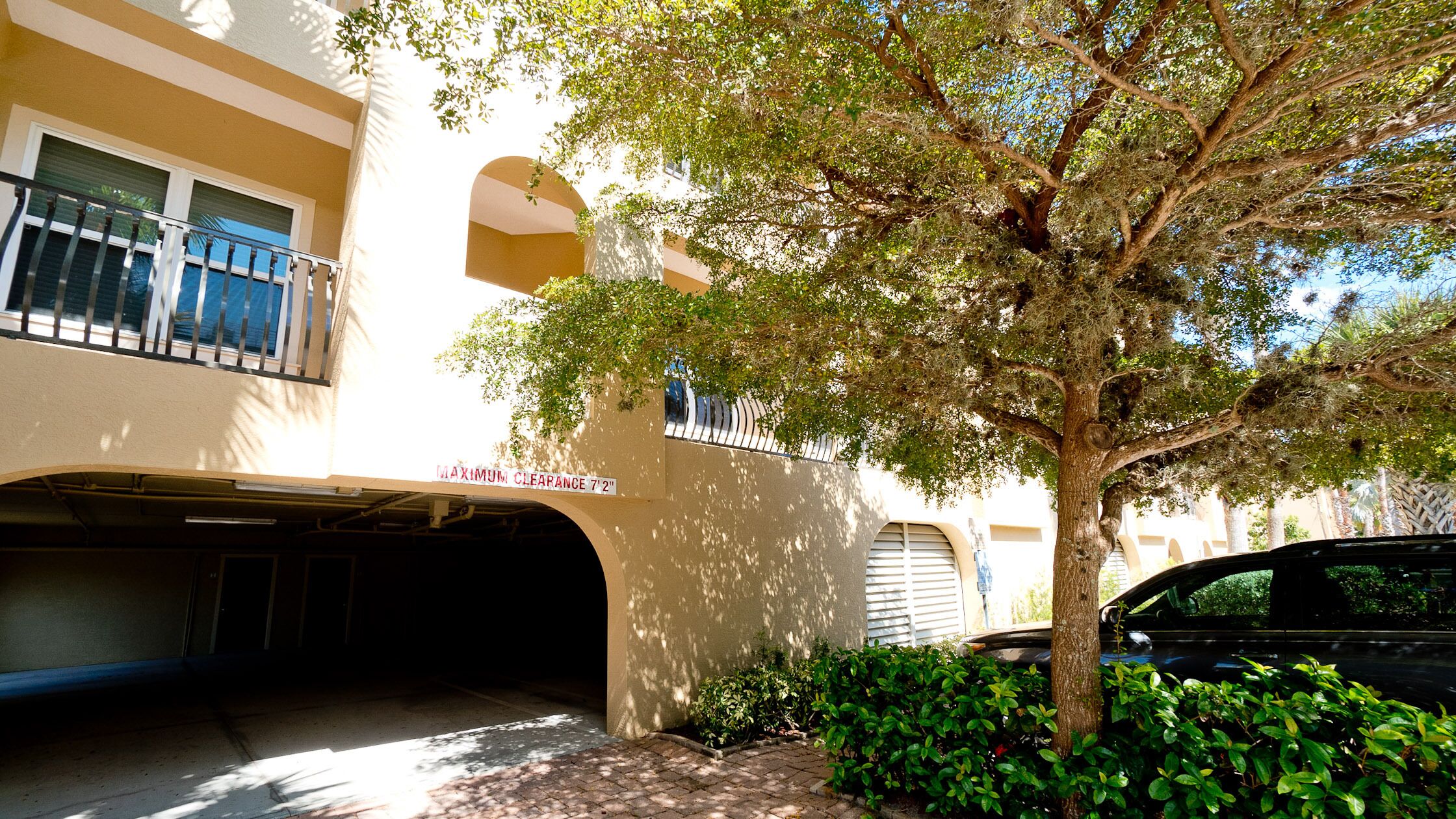 A building with a covered parking area, a tree, and a car parked nearby.