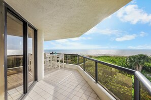 A balcony with a view of the ocean, a table with chairs, and a railing. - Stylish Beachfront Condo | Spa/Pool & Ocean Views (Marco Island)