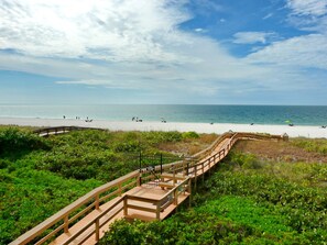 A wooden boardwalk leading to a beach with clear skies and calm waters.
