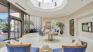 Un hall d’entrée spacieux, doté d’un haut plafond, de grandes fenêtres et d’un espace salon central avec des fauteuils bleus et une table ronde.