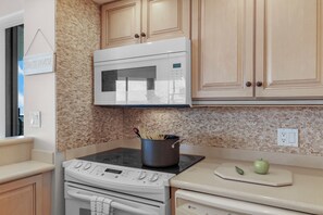 A kitchen with a microwave, oven, and a pot on the stovetop. - Stylish Beachfront Condo | Spa/Pool & Ocean Views (Marco Island)