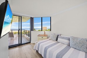 A bedroom with a large bed, a nightstand, and a view of the beach through a sliding door. - Stylish Beachfront Condo | Spa/Pool & Ocean Views (Marco Island)