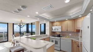 Une cuisine moderne dotée d’un grand îlot central, d’appareils électroménagers intégrés et offrant une vue sur l’extérieur.