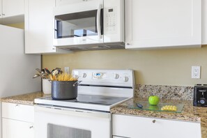 A kitchen with white cabinets, a microwave, an oven, and a granite countertop. - Front Unit Facing Beach | Wraparound Balcony (Marco Island)