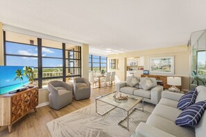A spacious living room with a large flat-screen TV, comfortable seating, and a view of the outdoors.
