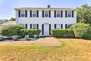 A two-story house with a front door, a brick pathway, and three potted plants.