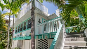 A two-story house with a balcony, a staircase, and a palm tree in the foreground. - Sail Away Cottage · 170 Steps · Pool · 1920's Cottage (Bradenton Beach)