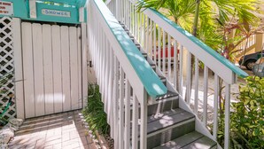 A staircase with a sign indicating a shower area, surrounded by greenery and a vehicle in the background. - Sail Away Cottage · 170 Steps · Pool · 1920's Cottage (Bradenton Beach)