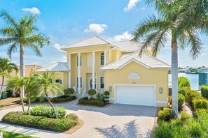 A two-story house with a white garage door, surrounded by palm trees and a well-maintained garden.