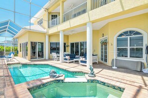 A pool area with a hot tub, lounge chairs, and a covered patio.