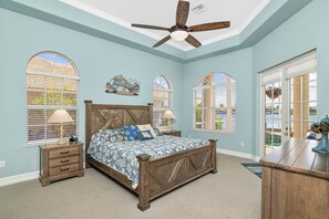 A bedroom with a wooden bed, two nightstands, a ceiling fan, and large arched windows.