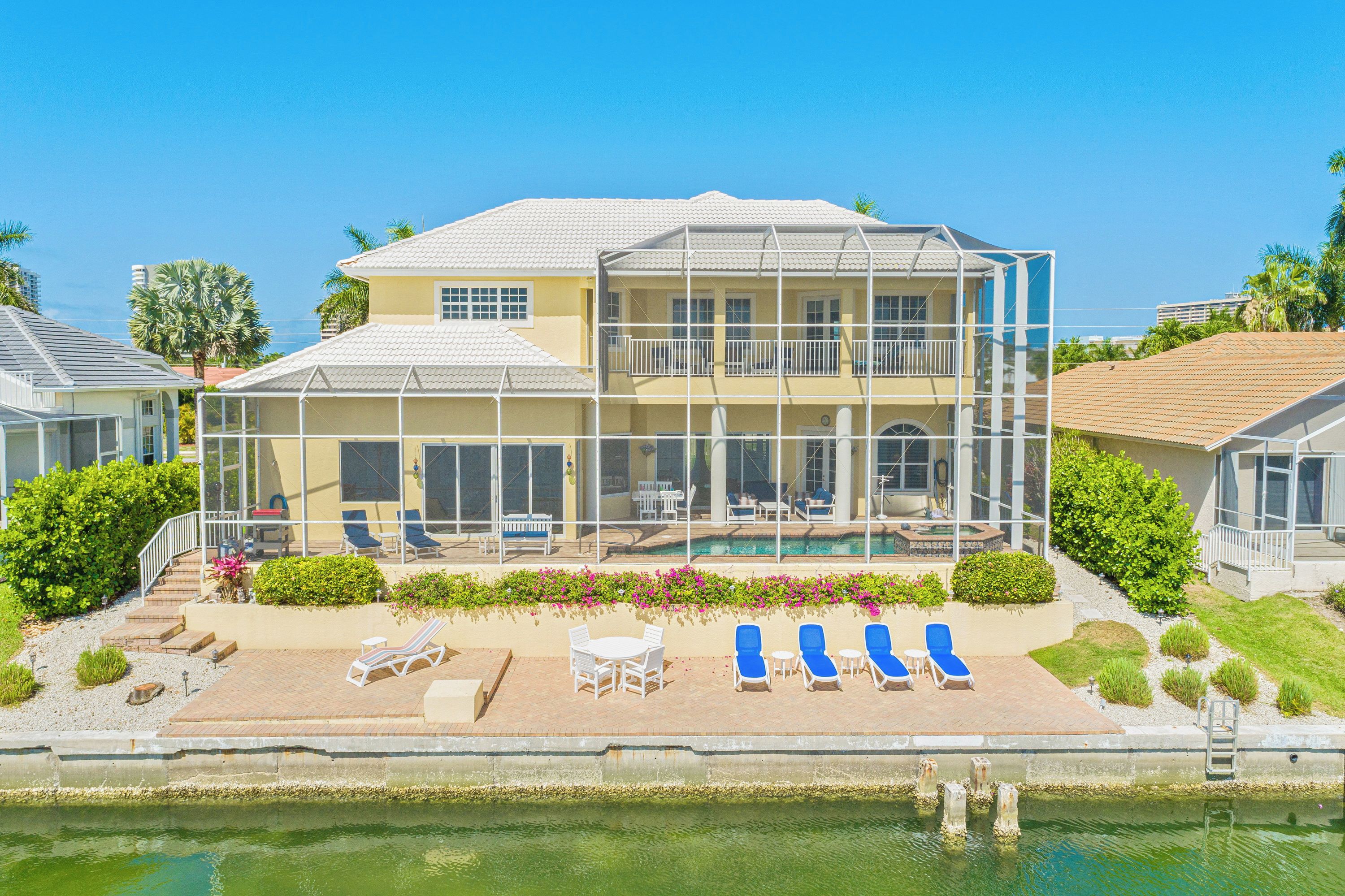 A two-story house with a pool, outdoor seating, and a view of the ocean.