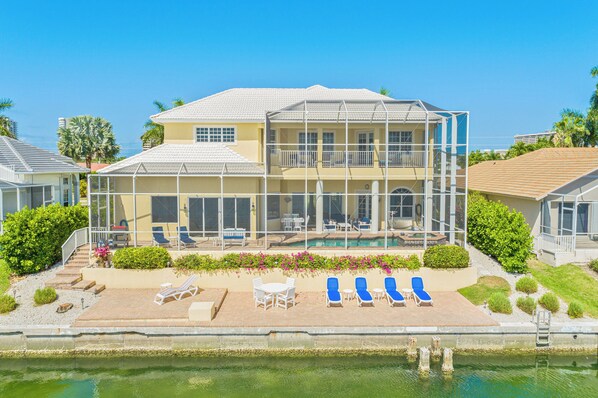 A two-story house with a pool, outdoor seating, and a view of the ocean.
