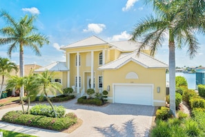 A two-story house with a white garage door, surrounded by palm trees and well-maintained landscaping.
