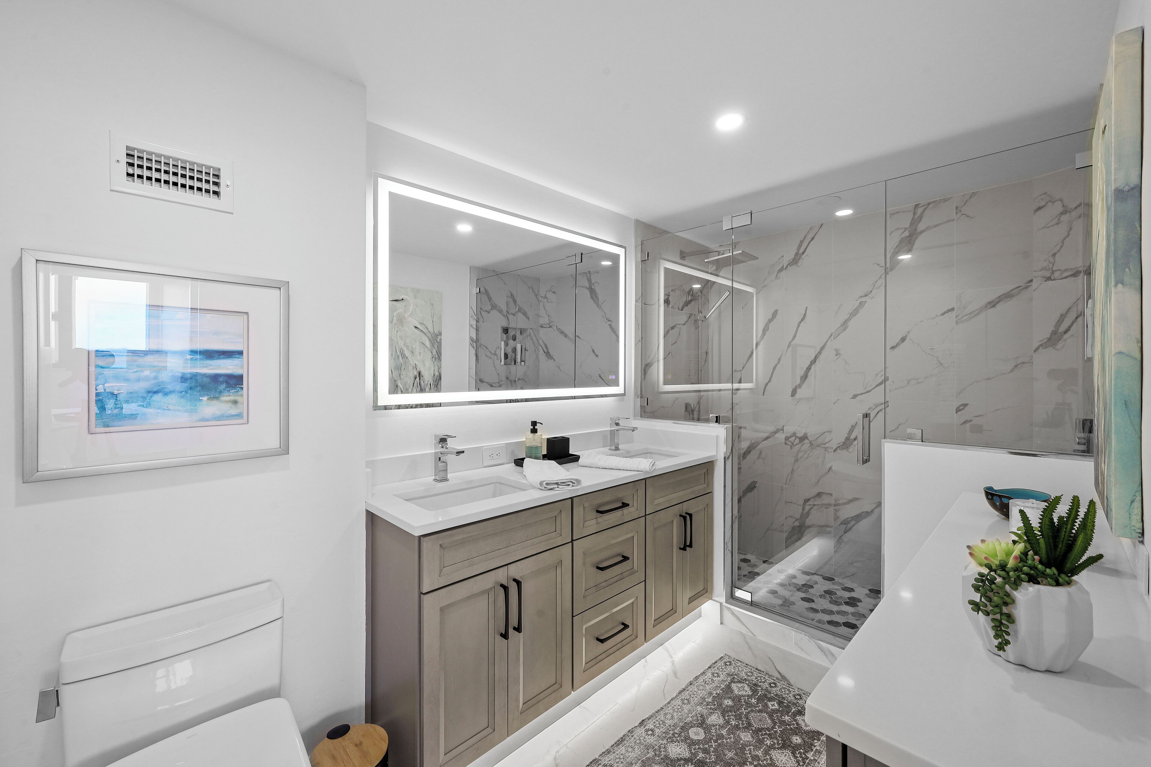A modern bathroom with a marble shower, a large mirror, and a framed picture on the wall.