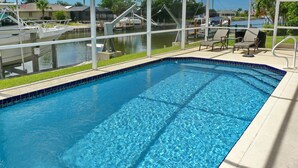 Una piscina con agua cristalina azul, rodeada por una zona techada con sillas y vistas a barcos y casas.