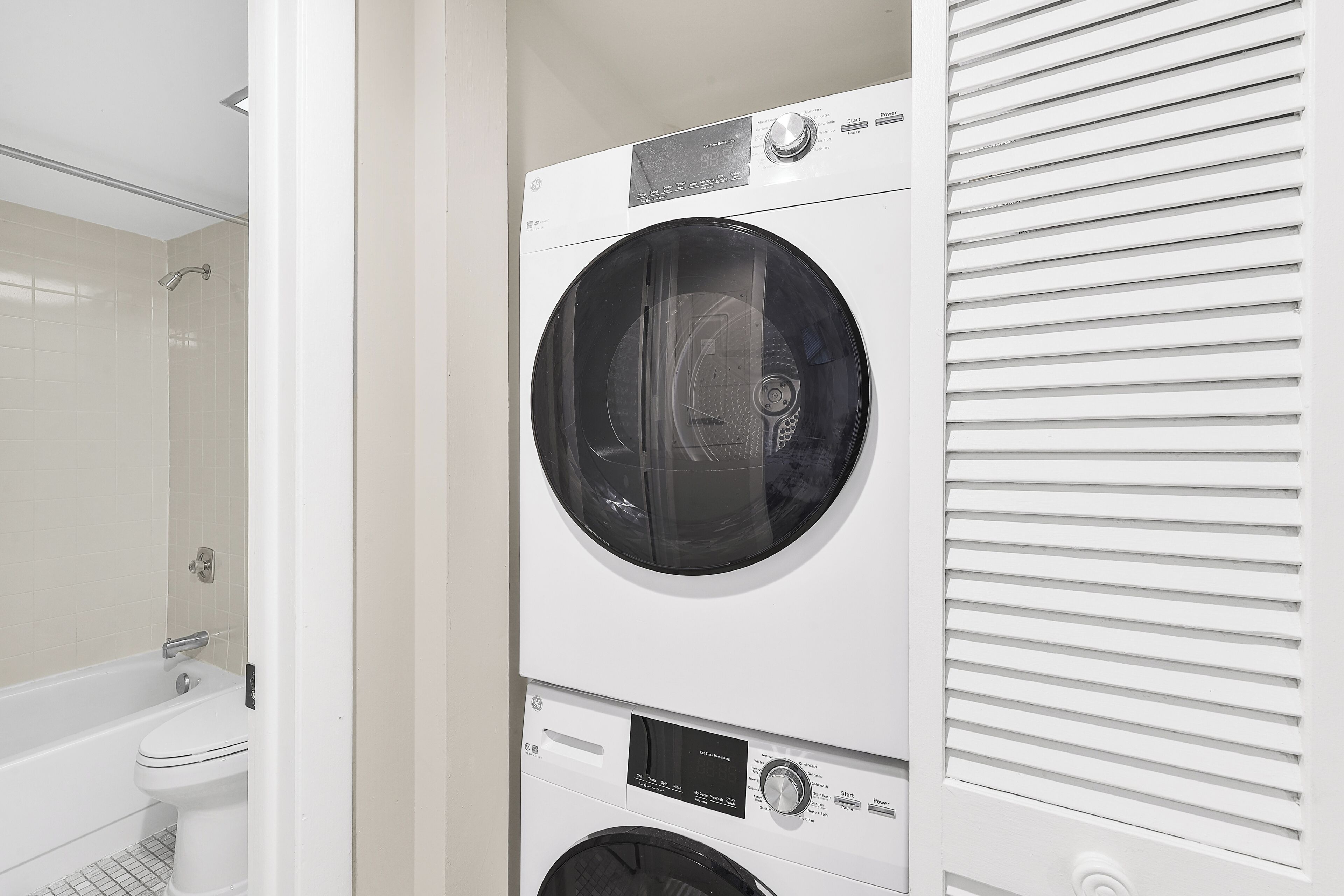 A stacked washer and dryer unit in a bathroom with a visible shower area.
