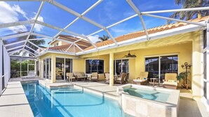 Una piscina techada con sillones de descanso y un ventilador de techo, rodeada de paredes amarillas y ventanas amplias.