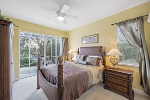A bedroom with a bed, two bedside tables with lamps, a ceiling fan, and a window with curtains.