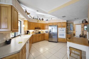 A kitchen with wooden cabinets, a stainless steel refrigerator, and a large island with a sink.