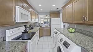 A modern kitchen with wooden cabinets, a microwave, stove, and a washing machine. - South End Condo | Pool, Spa and Steps to Beach (Marco Island)