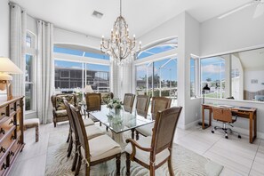 Un comedor amplio con una mesa de vidrio, rodeado de sillas de madera, un candelabro y grandes ventanales que dan al exterior.