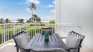 Ein Balkon mit Tisch und Stühlen, der Blick auf einen Strand mit Palmen und das Meer freigibt.
