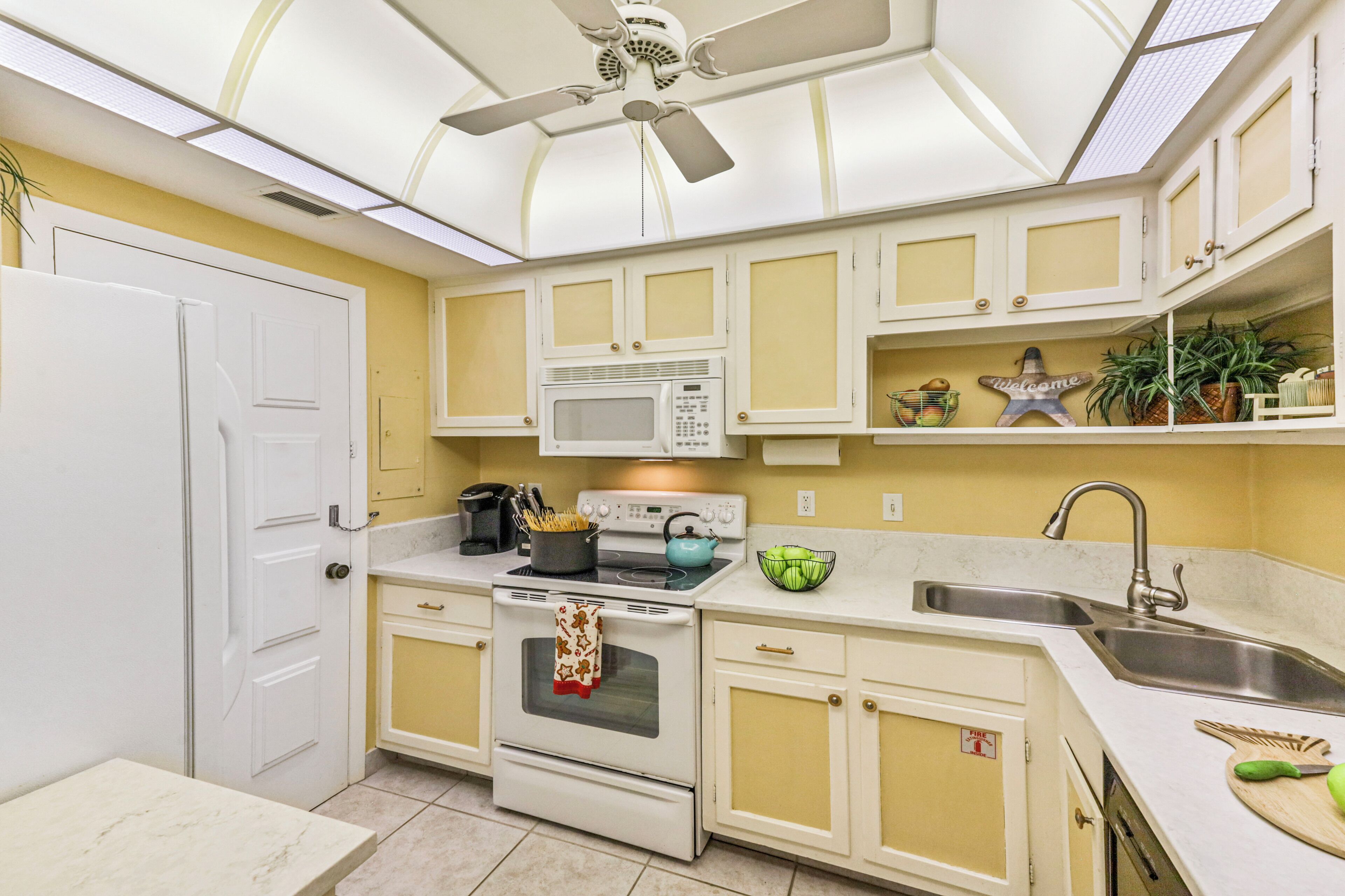 Et køkken med hvide skabe, en mikroovn, en komfur og en loftventilator.