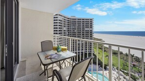 Een balkon met een tafel, stoelen en uitzicht op een strand en hotel.