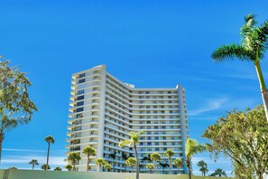 A multi-story hotel with balconies, surrounded by palm trees. - Eye-Catching Beachfront Condo | Pool & Nice Views (Marco Island)