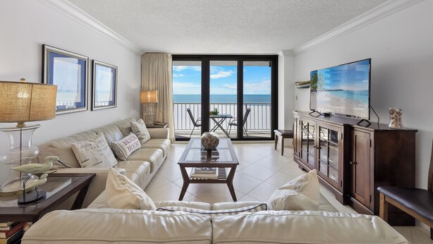 Een ruime woonkamer met een groot raam en uitzicht op zee, een comfortabele bank, een bijzettafeltje en een televisie.