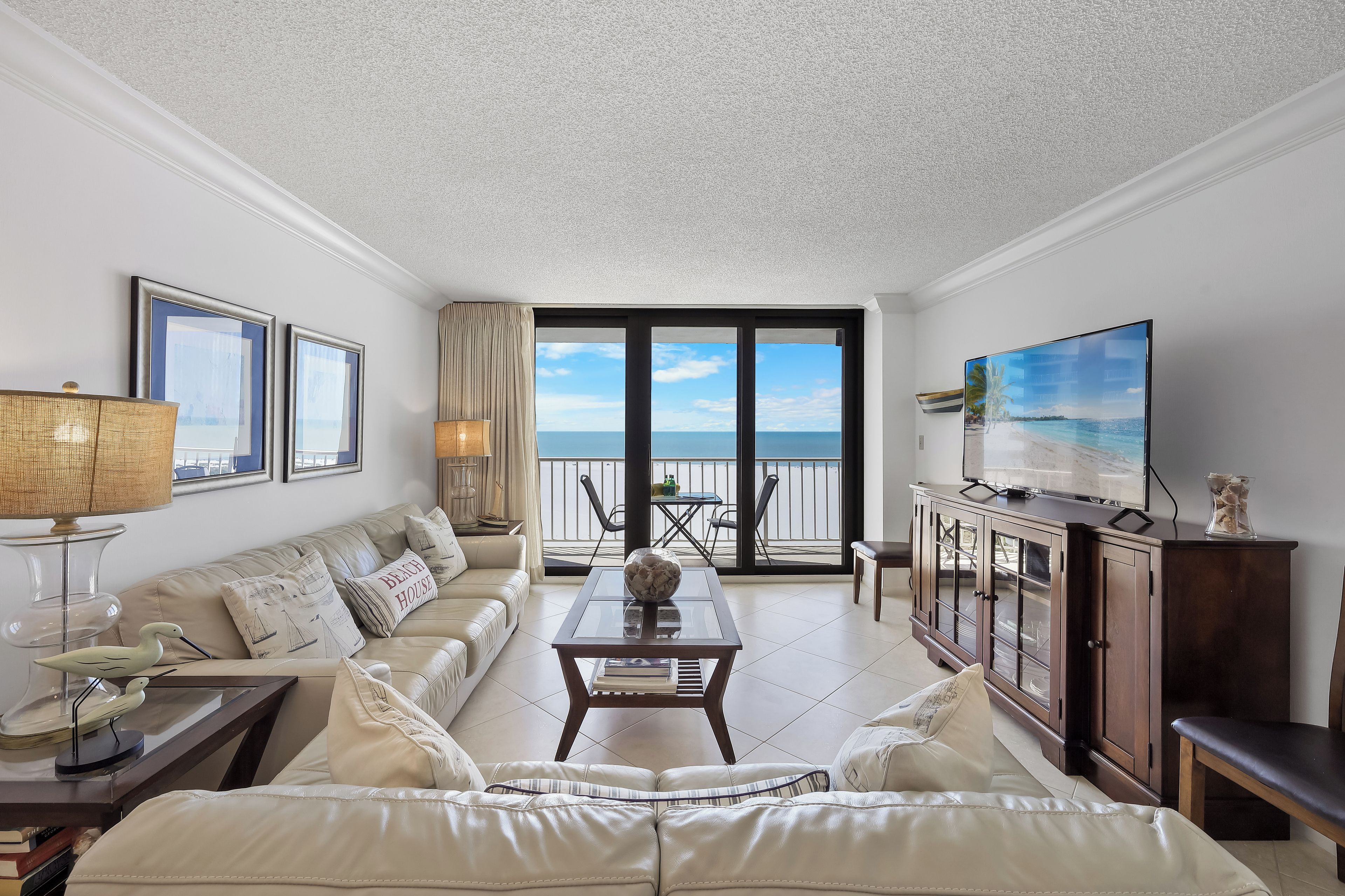 A spacious living room with a large window offering a view of the sea, a comfortable sofa, a coffee table, and a television.