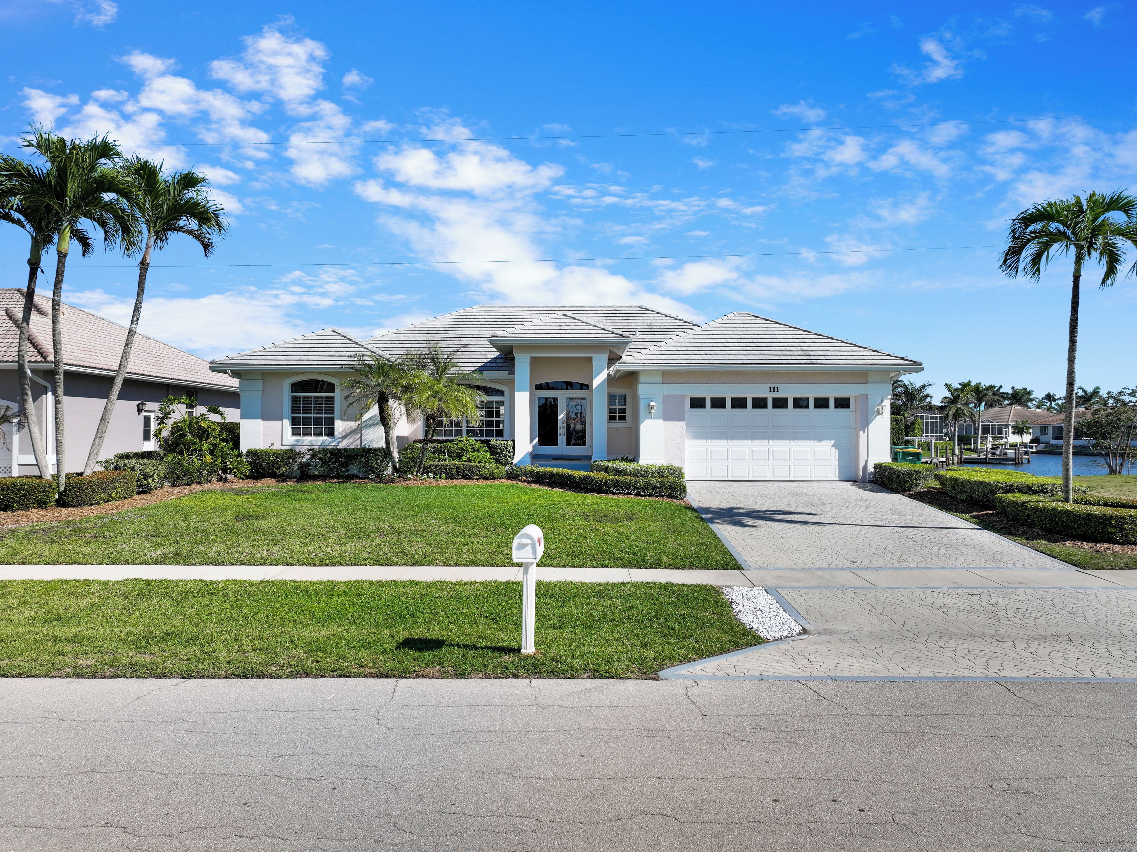 A single-story house with a garage, a well-maintained lawn, and palm trees.