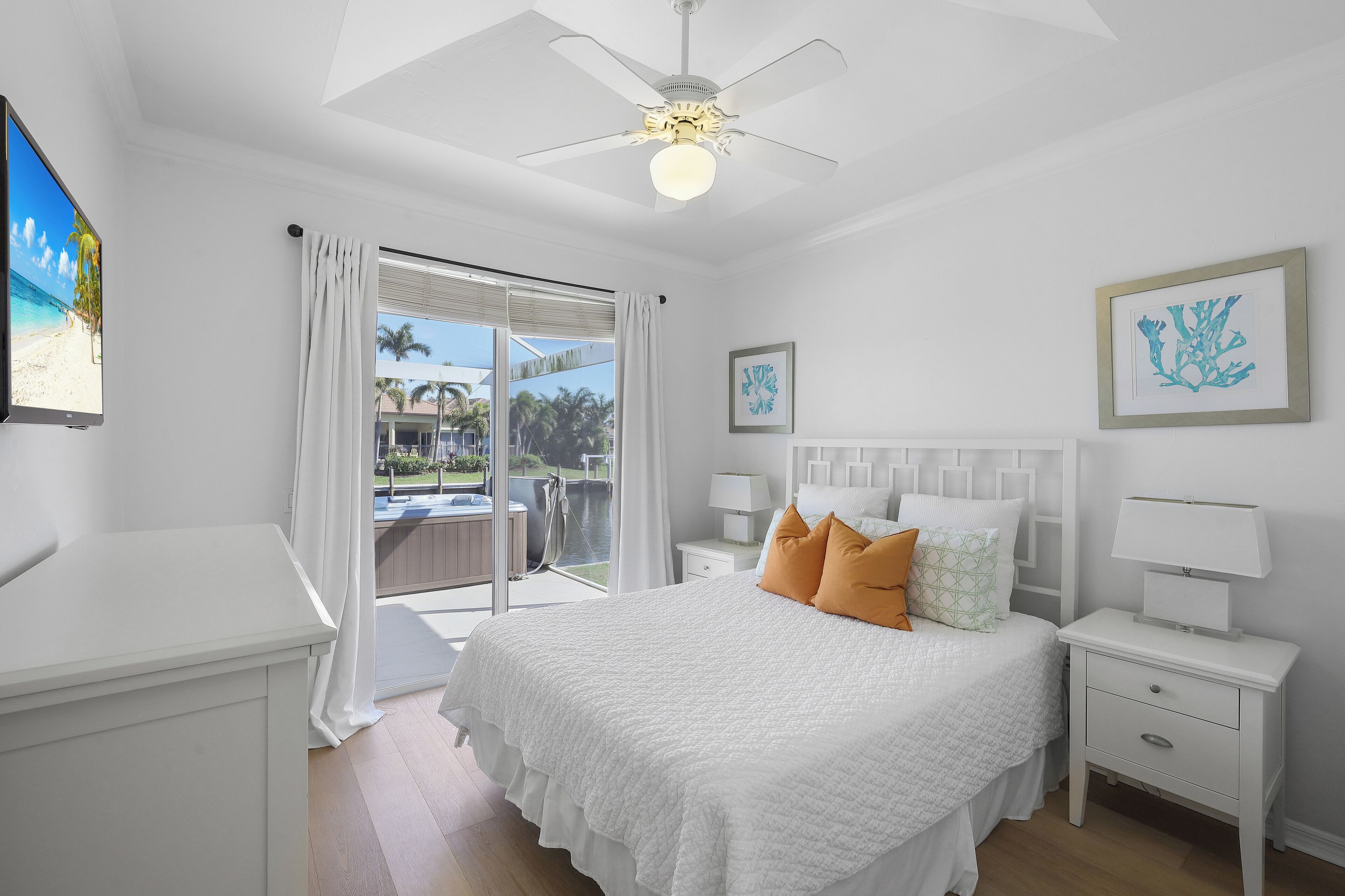 A bedroom with a bed, nightstands, a ceiling fan, and a view of the outdoors.