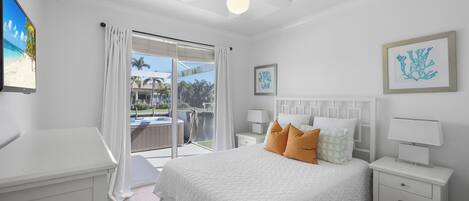 A bedroom with a bed, nightstands, a ceiling fan, and a view of the outdoors.